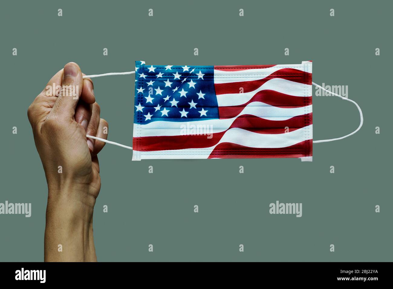 Primo piano di uomo che tiene una maschera chirurgica modellata con la bandiera degli Stati Uniti su uno sfondo grigio Foto Stock