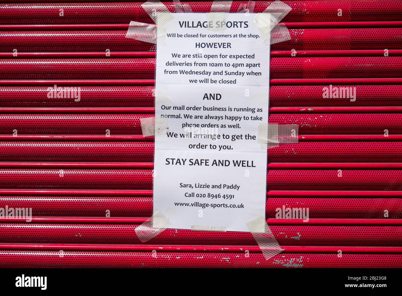 Un otturatore rosso con un cartello con scritto a esso che dice ai clienti che, anche se il negozio è chiuso consegna a casa è ancora disponibile. Foto Stock