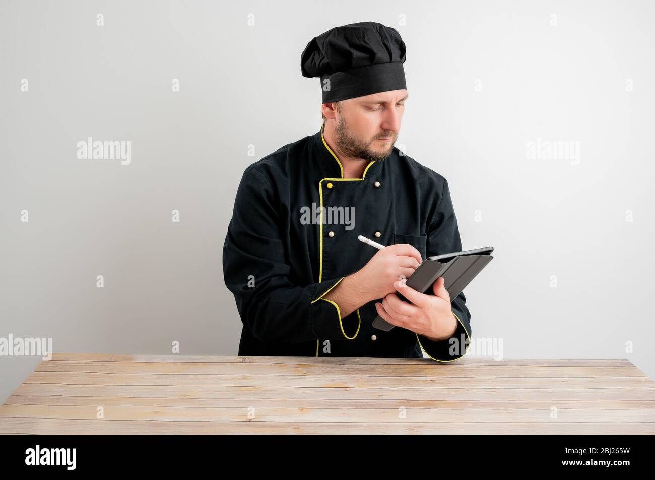Ritratto di giovane cuoco maschile in uniforme nera prende appunti, posando su uno sfondo bianco isolato Foto Stock