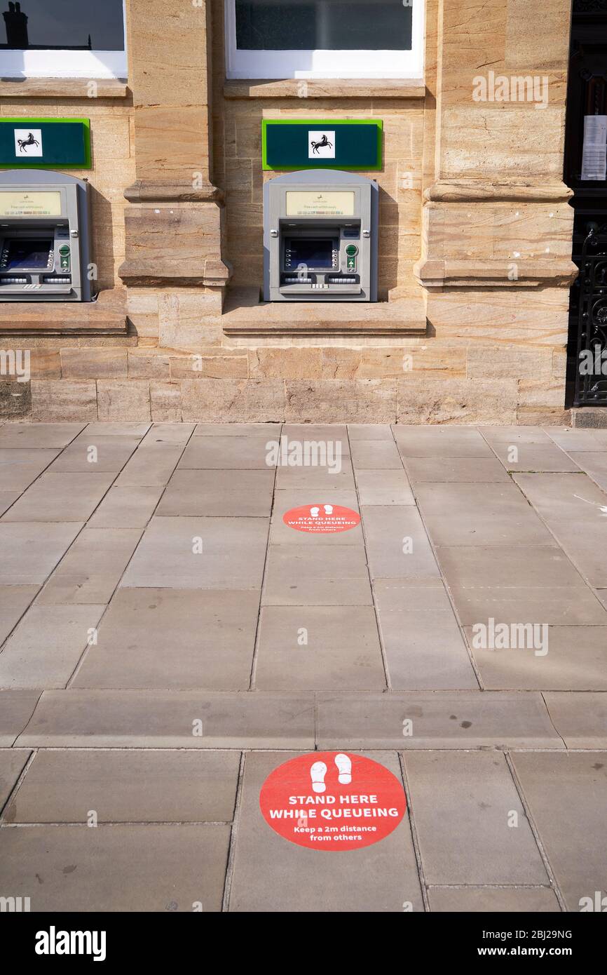Adesivi rossi di istruzioni di divaricamento sociale su marciapiede che portano a bancomat Foto Stock