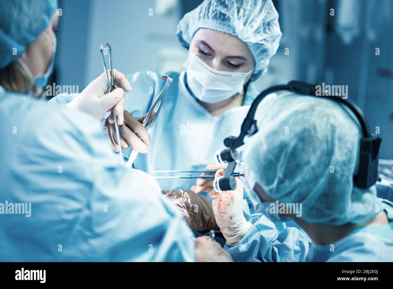 Chirurgo femminile con assistenti operativi. Chirurghi durante il lavoro. Filtro blu. Medicina moderna con medici professionisti. Foto Stock