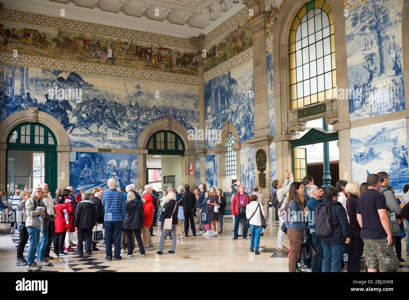 Turisti che ammirano le famose piastrelle azulejos tradizionali portoghesi blu e bianco parete stazione ferroviaria Sao Bento a Porto, Portogallo Foto Stock