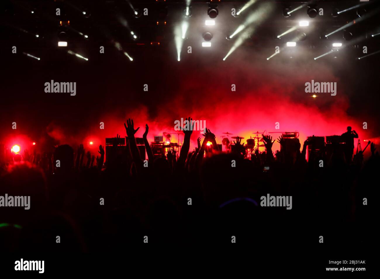 Udienza con le mani sollevate a un festival di musica e luci streaming verso il basso a partire da sopra il palcoscenico. Soft focus, ISO elevata, immagini sgranate. Foto Stock