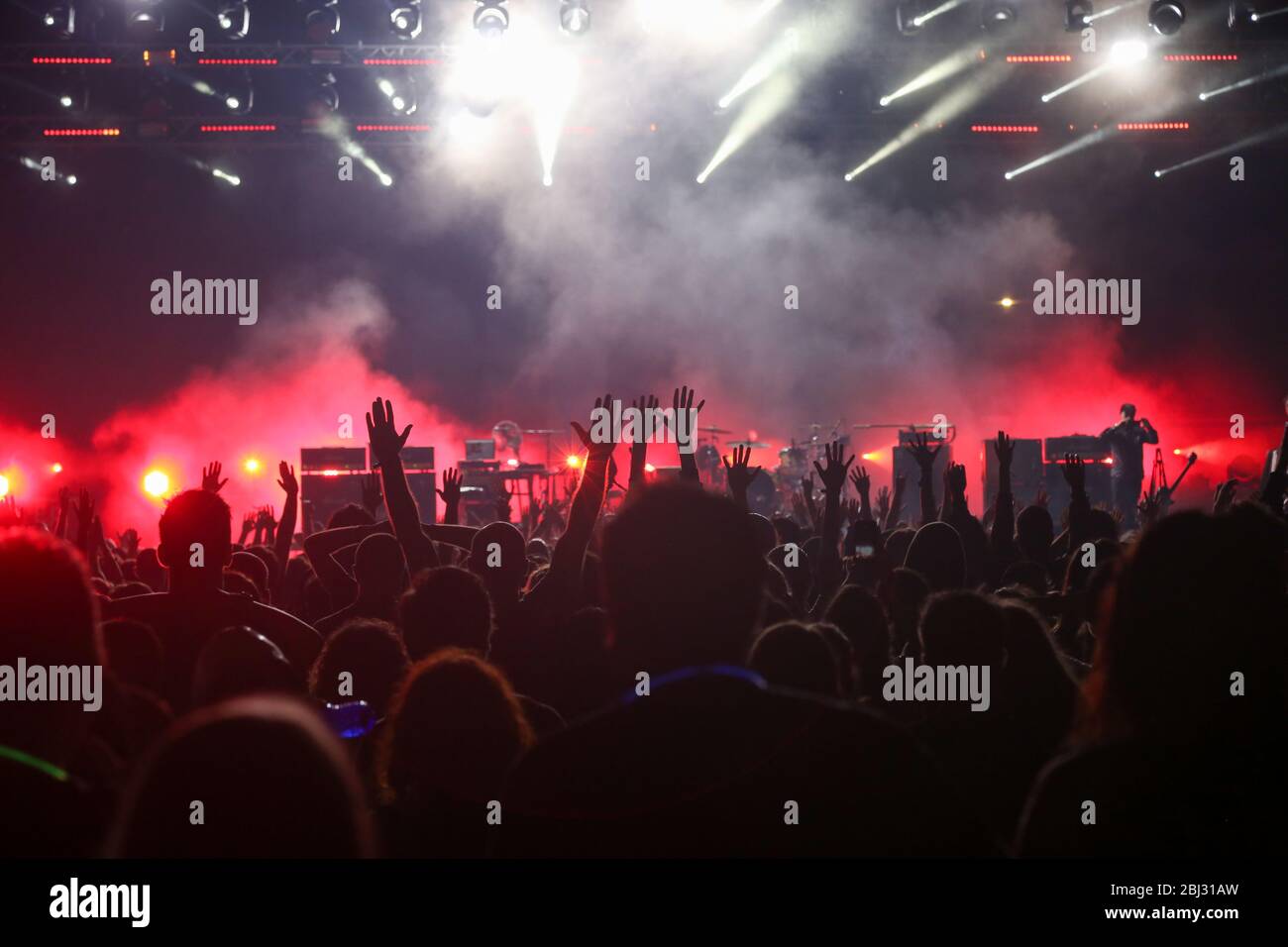 Udienza con le mani sollevate a un festival di musica e luci streaming verso il basso a partire da sopra il palcoscenico. Soft focus, ISO elevata, immagini sgranate. Foto Stock