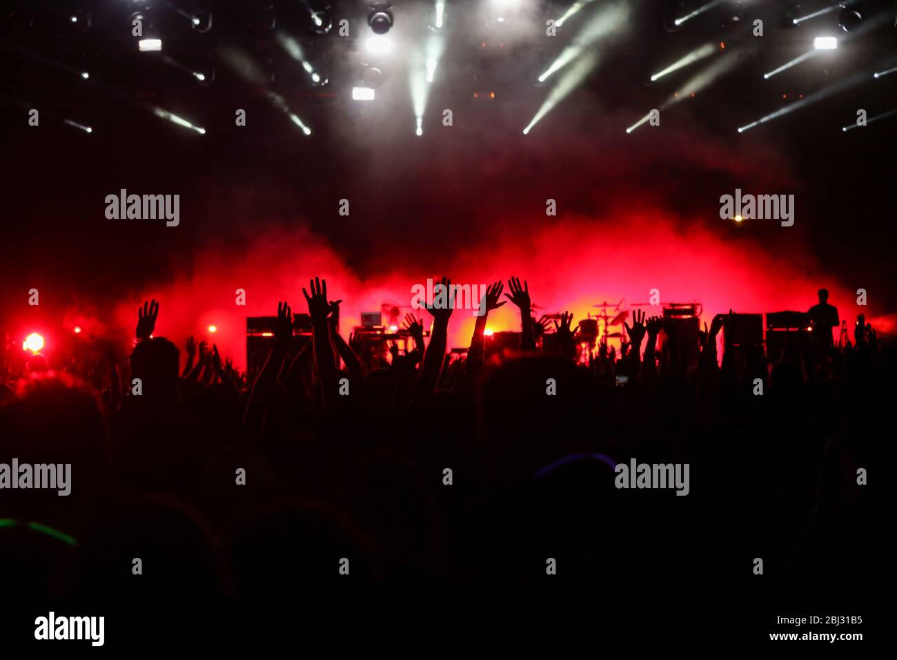 Udienza con le mani sollevate a un festival di musica e luci streaming verso il basso a partire da sopra il palcoscenico. Soft focus, ISO elevata, immagini sgranate. Foto Stock