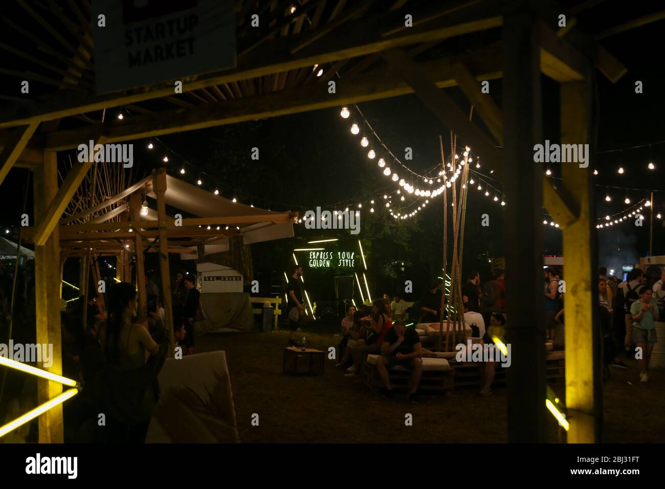Udienza con le mani sollevate a un festival di musica e luci streaming verso il basso a partire da sopra il palcoscenico. Soft focus, ISO elevata, immagini sgranate. Foto Stock
