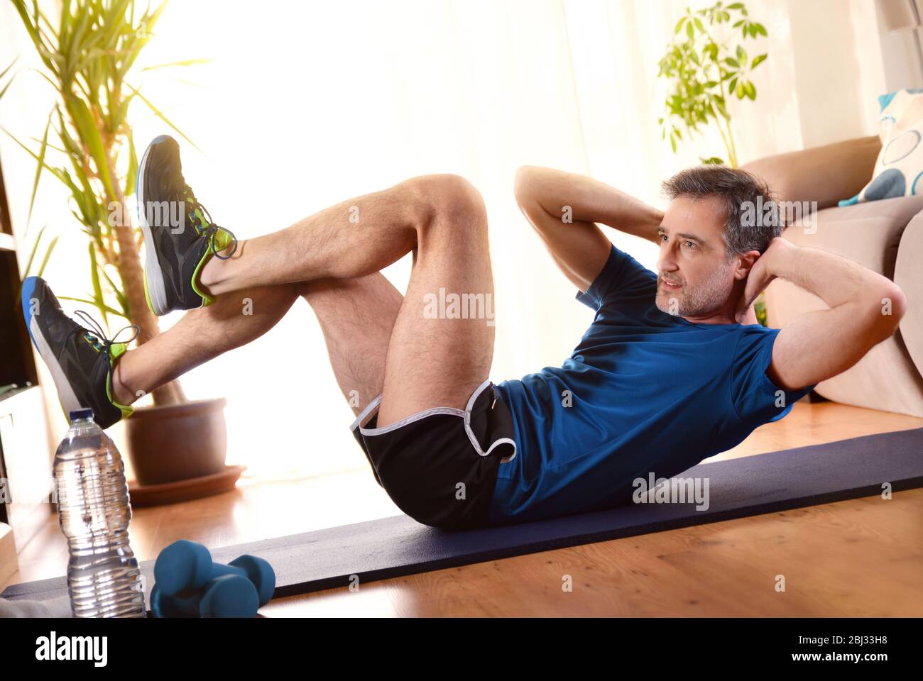 Uomo che fa esercizi addominali e gambe nel soggiorno a casa sdraiato su un  tappetino Foto stock - Alamy