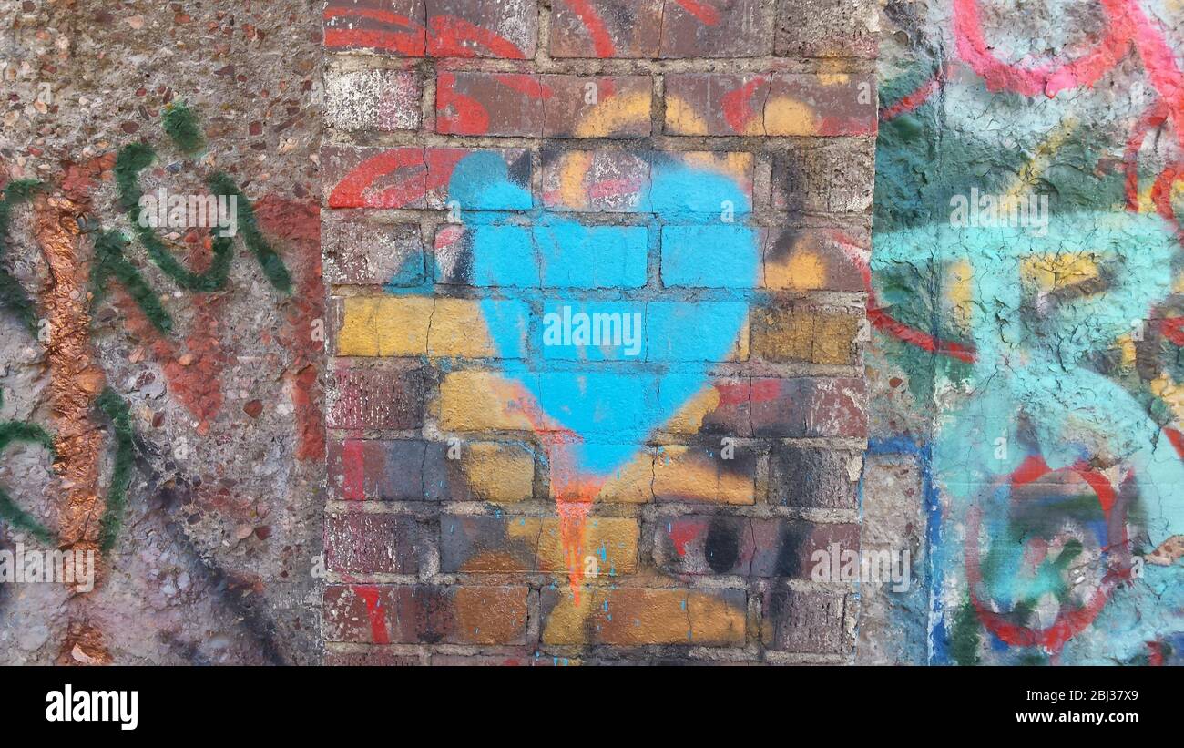 Un edificio abbandonato in disuso con tre diverse strutture sulle sue vecchie pareti e un cuore di graffiti dipinto sui mattoni a camino Foto Stock