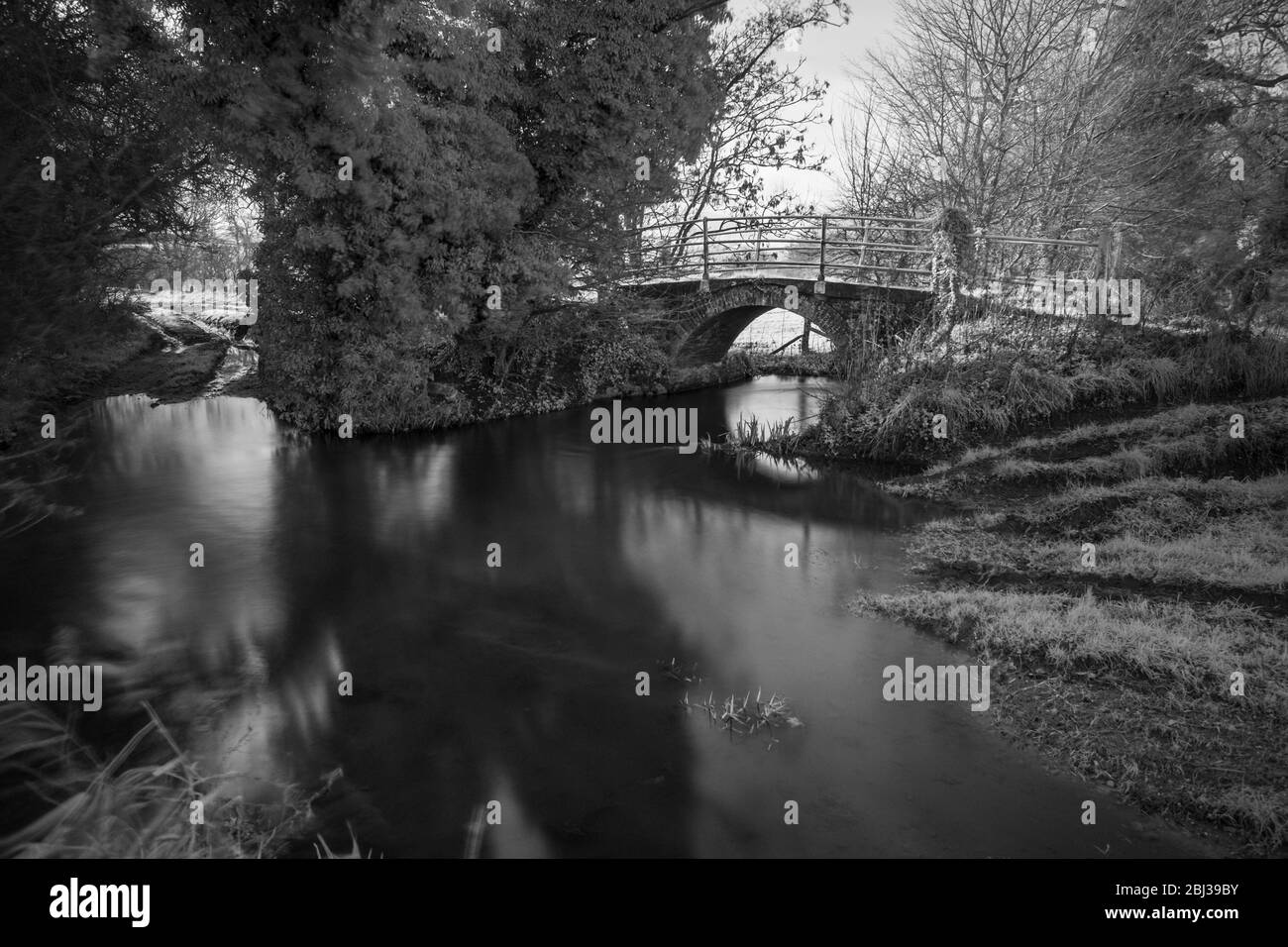Ponte pedonale in mattoni sul fiume Stiffkey, Norfolk, Inghilterra. Immagine a infrarossi in bianco e nero. Foto Stock