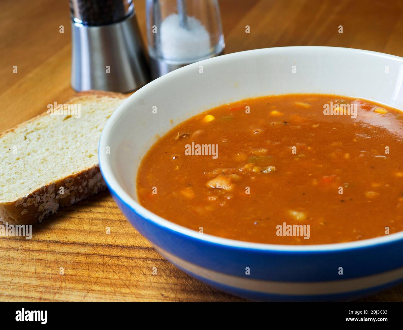 Una ciotola di zuppa di tre fagioli con una fetta di pane fatto in casa su un'asse di legno Foto Stock