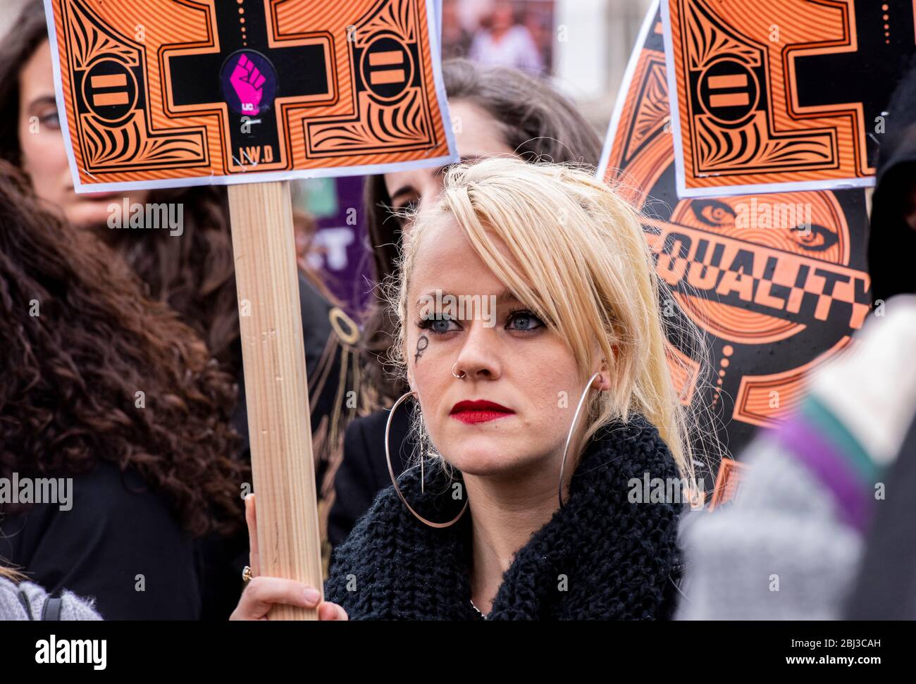 Una giovane donna di grande impatto con orecchini e rossetto rosso si unisce alla folla in Piazza del Parlamento per celebrare la Giornata internazionale della donna. Foto Stock