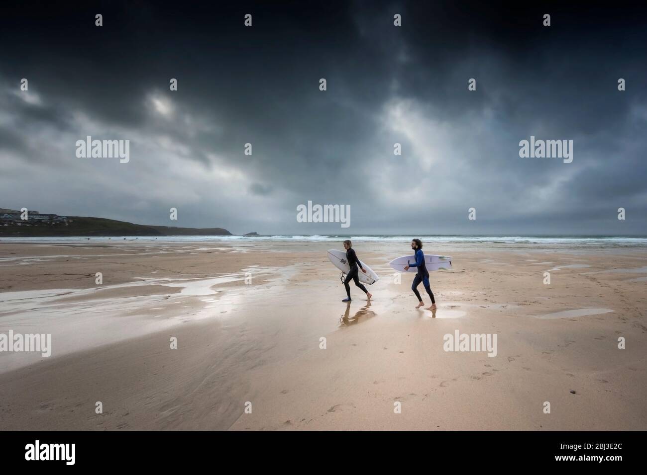 I surfisti che camminano sulla spiaggia Fistral, mentre le nuvole buie e buie della tempesta si avvicinano a Newquay in Cornovaglia. Foto Stock