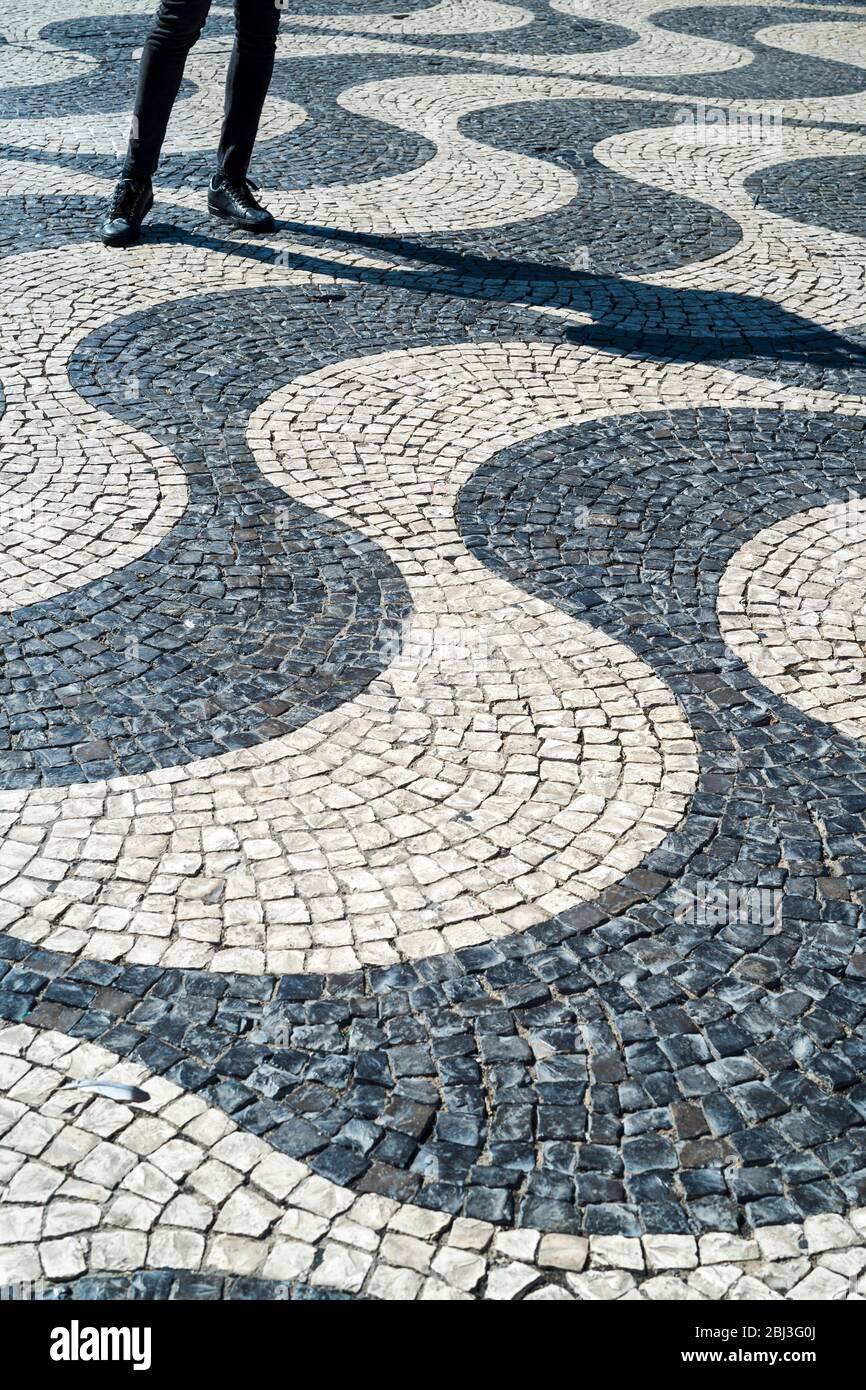 Allungare l'ombra di un uomo su paviers formando linee ondulate e disegni geometrici in Piazza Rossio a Lisbona, Portogallo Foto Stock