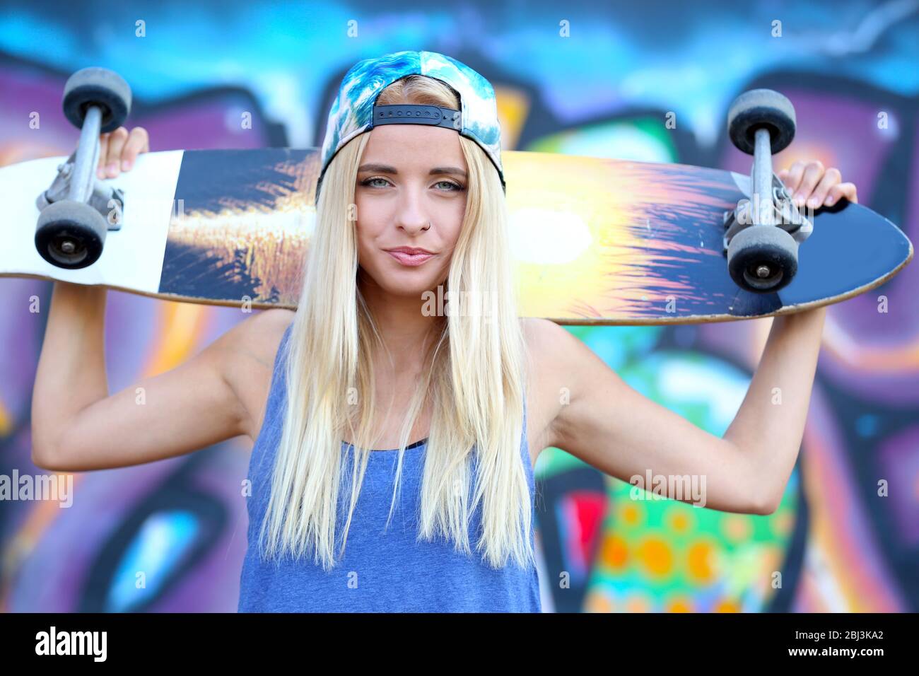 Giovane donna con skating board su sfondo muro dipinto Foto Stock