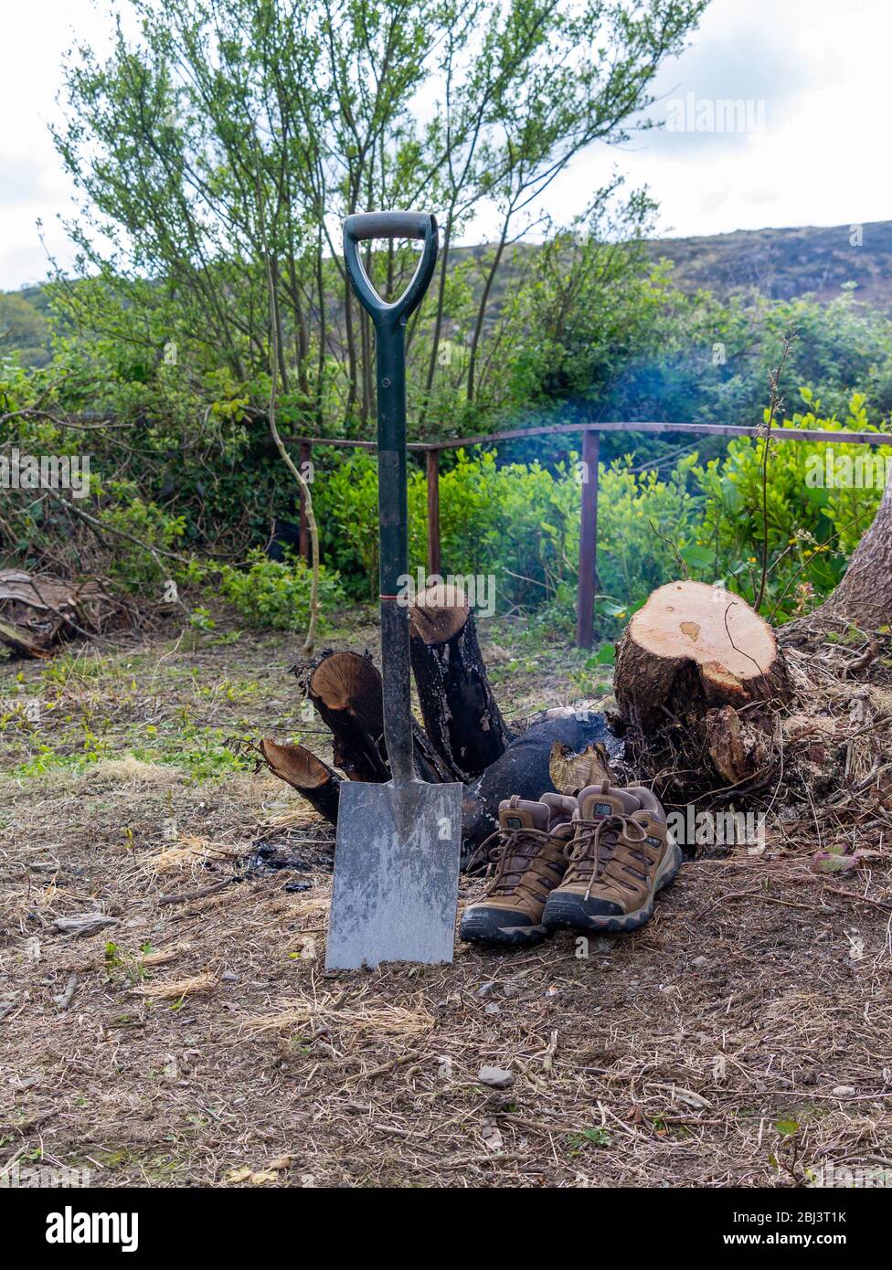 Il giardino ha spiovato o pala con un paio di scarpe accanto ad un ceppo di albero bruciato. Foto Stock