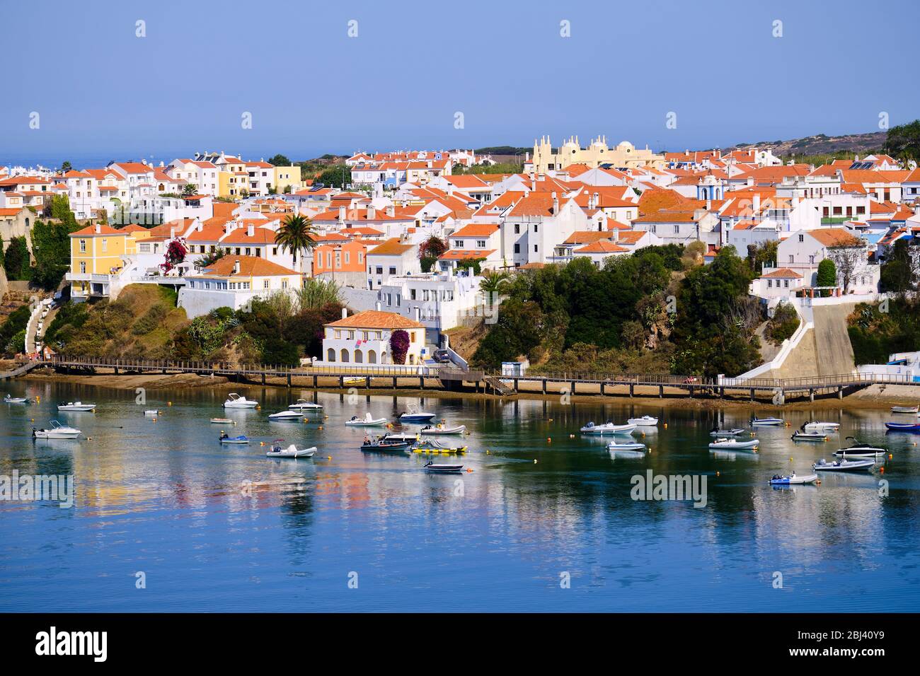 La città Vila Nova de Milfontes si riflette nelle acque del porto pieno di barche. Trekking con Backpacker solo sulla Rota Vicentina e pescatori Foto Stock