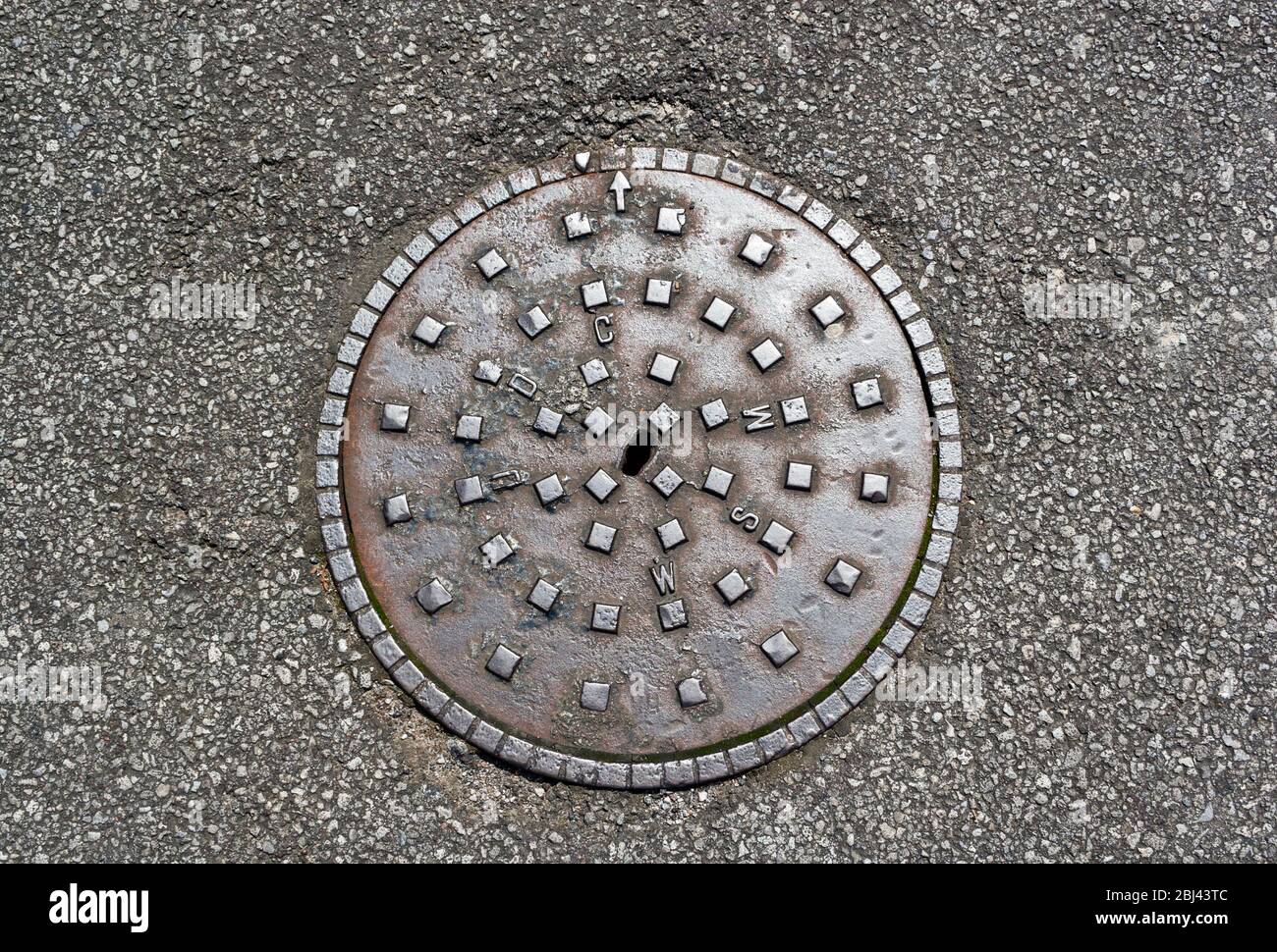 Un manhole in ghisa a Weston-super-Mare, Regno Unito, recante le iniziali del Weston-super-Mare Urban District council, un'autorità locale che cessò di essere Foto Stock