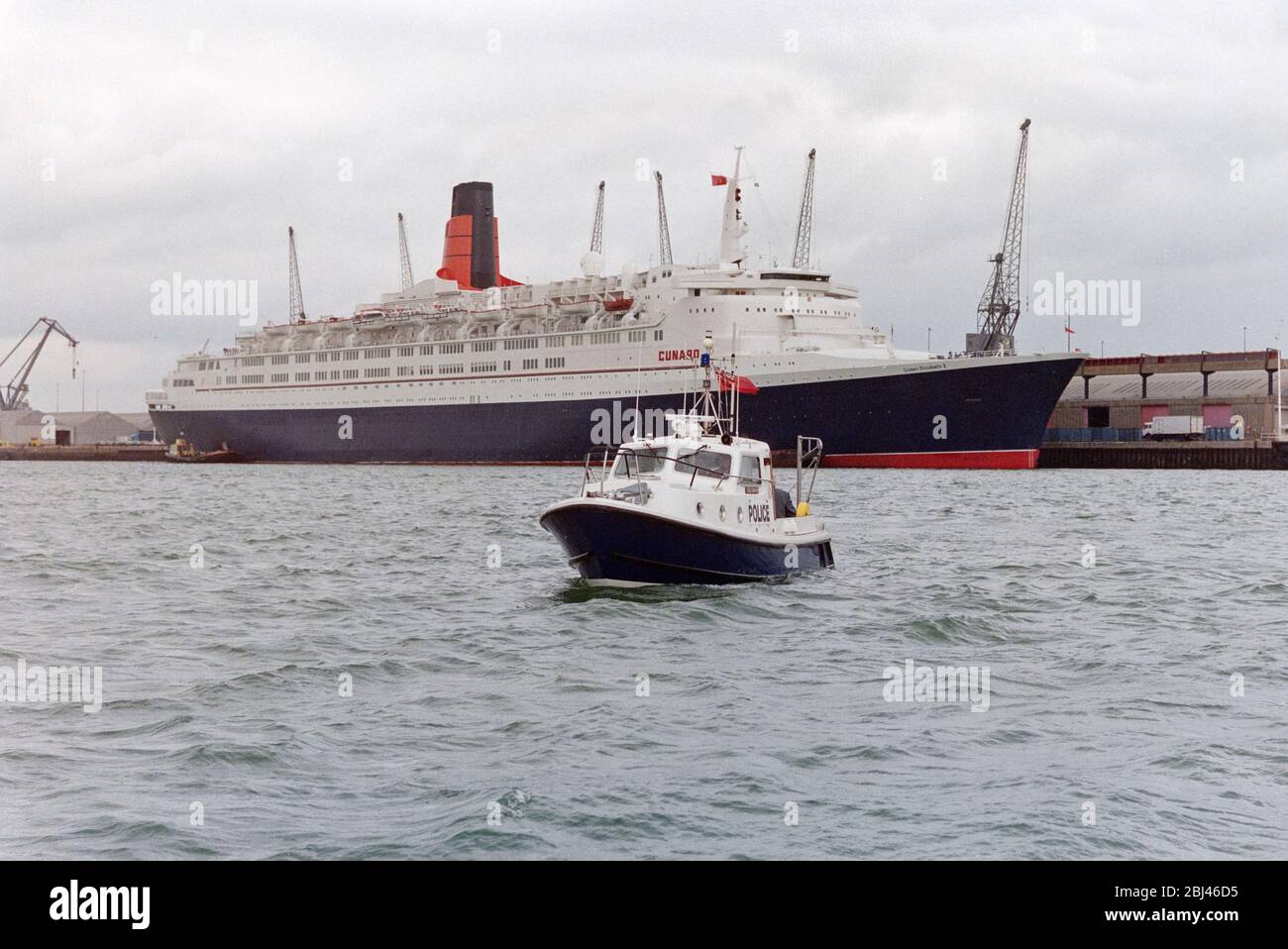 Foto d'epoca della Regina Elisabetta 2 ormeggiata a Porto di Southampton con la polizia Hampshire lancio marino Lord Ashburton in primo piano. Foto Stock