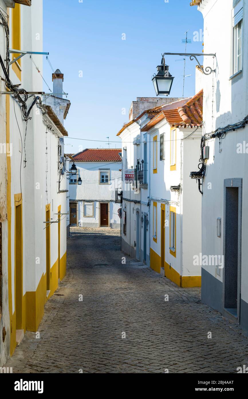 Tipiche case bianche e gialle e lanterne in stretta strada di ciottoli a Evora, Portogallo Foto Stock