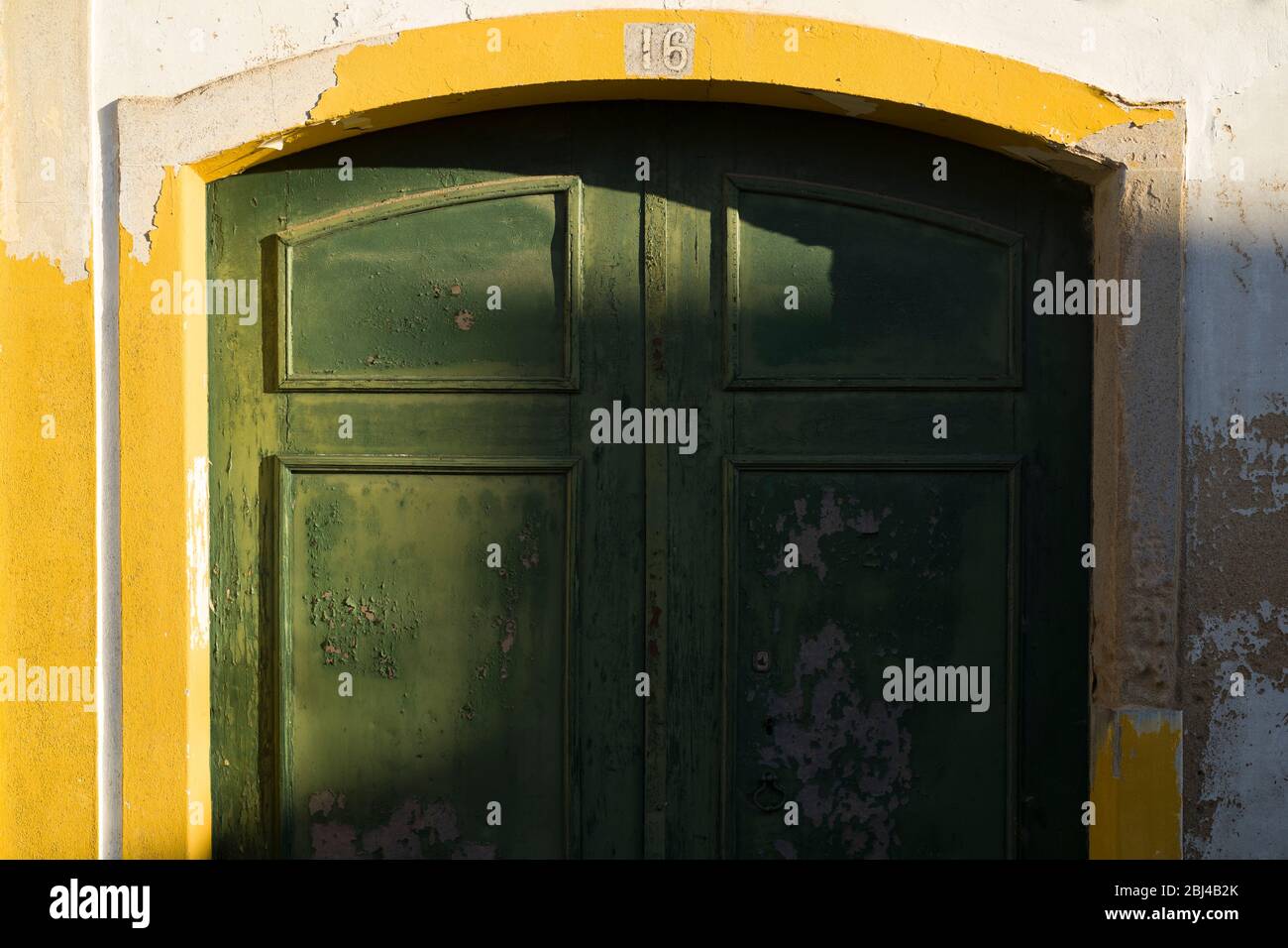 Luce e ombra su tipica casa bianca e gialla con porta verde a Evora, Portogallo Foto Stock
