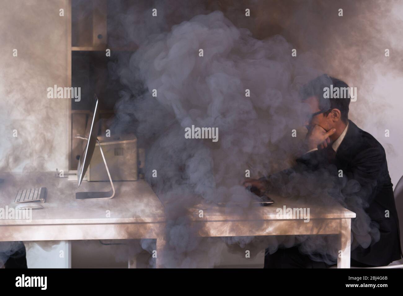 Primo piano di incendi che si bruciano all'interno della cabina dell'ufficio durante i lavori. Uomo lavoratore in ufficio in un fuoco. Concetto di cortocircuito e incidenti. SOS e salvare vite. Foto Stock