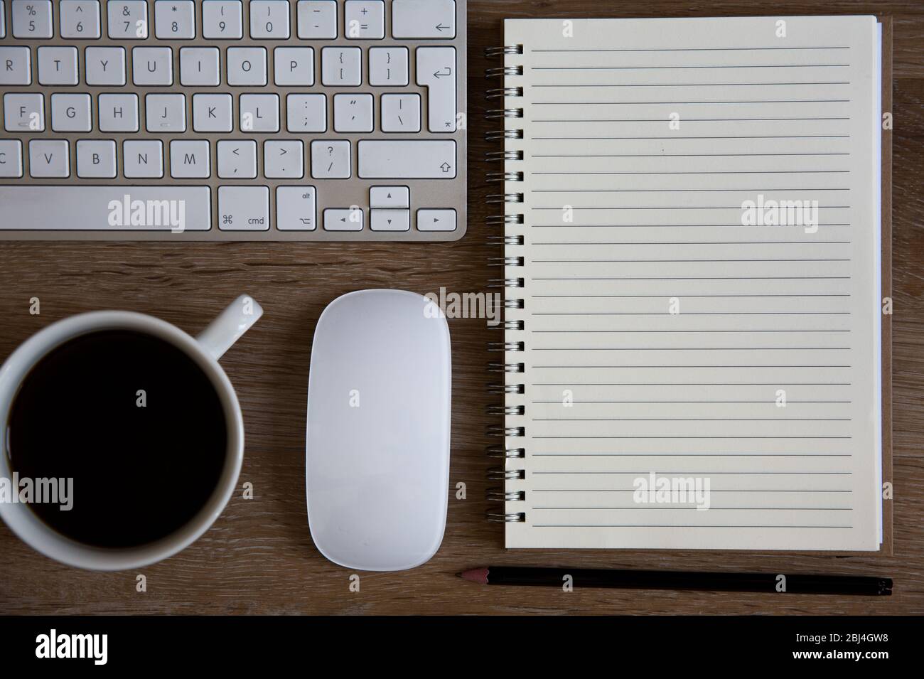 Una vista ad angolo elevato di una scrivania da ufficio con tastiera, caffè, mouse e notebook a spirale con spazio per le copie foderato per le note Foto Stock