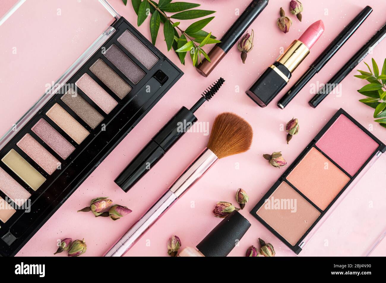 Make up cosmetici naturali piatto lay. Rossetto e smalto per unghie, ombre degli occhi e arrossire, pennelli, matite e boccioli di rosa sullo sfondo di colore rosa. Foto Stock