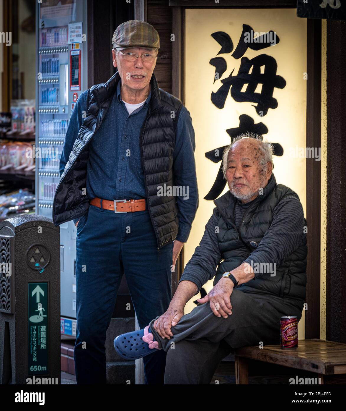 Due uomini giapponesi anziani locali che guardano le persone che passano e parlano. Enoshima, la principale via dello shopping, Enoshima Island, Giappone Foto Stock