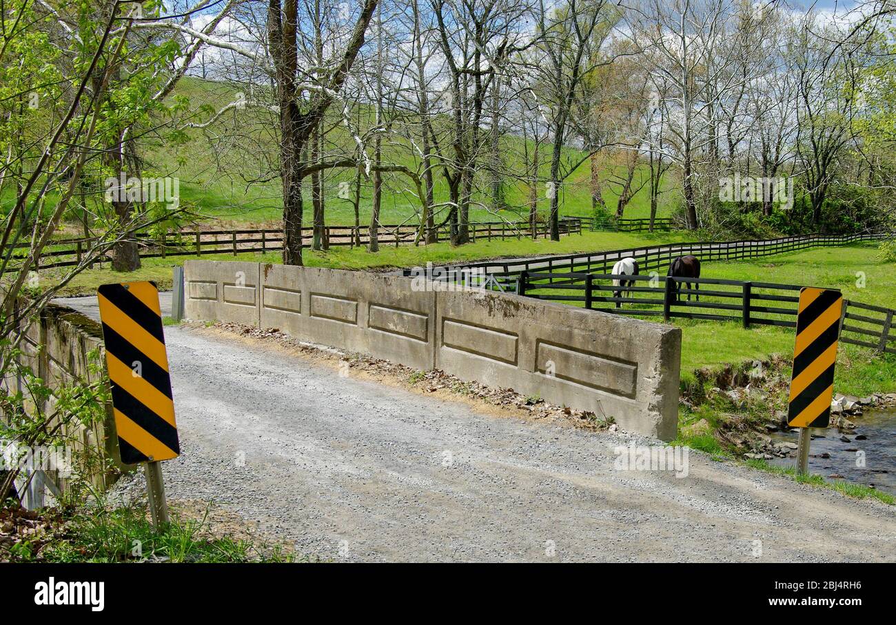 Piccolo Country Bridge: Una strada di ghiaia stretta attraversa un ponte a una corsia e passa accanto a un allevamento di cavalli nella Virginia occidentale. Foto Stock