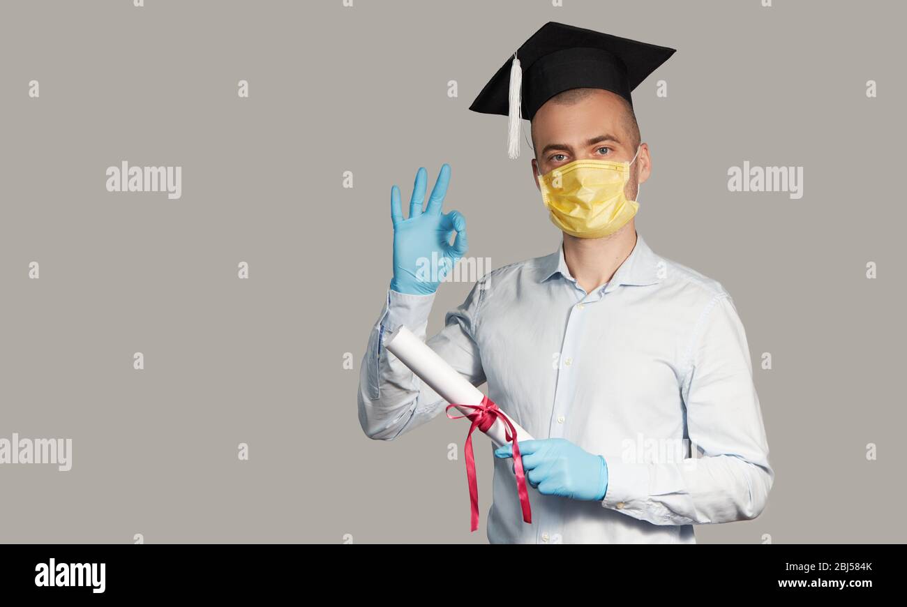 Laurea in liceo durante una quarantena. Studente laureato in un cappello e una maschera protettiva ha un diploma Foto Stock