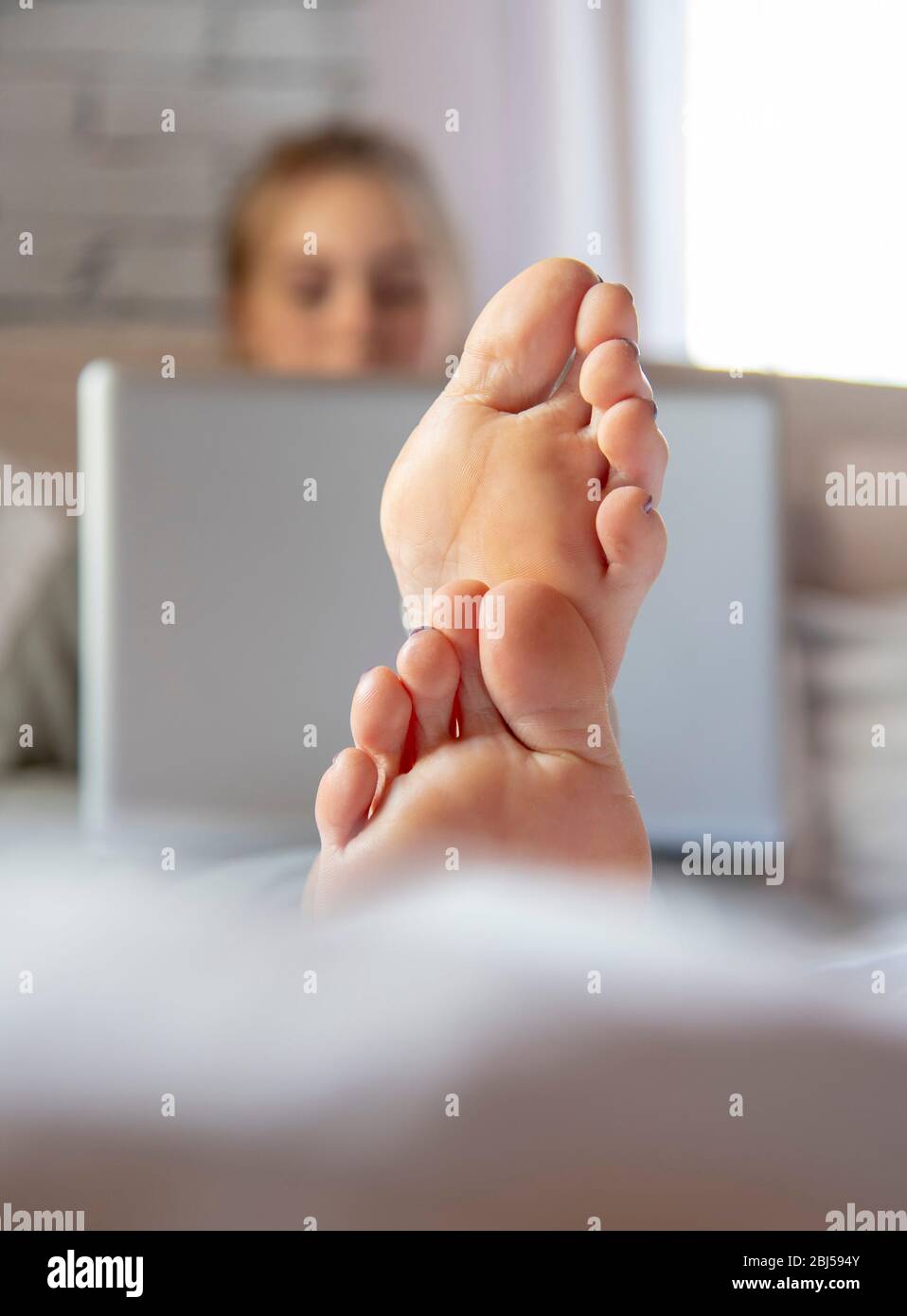 Mettere a fuoco i piedi in primo piano. Una ragazza adolescente è sdraiata su un letto con un computer portatile. Foto Stock