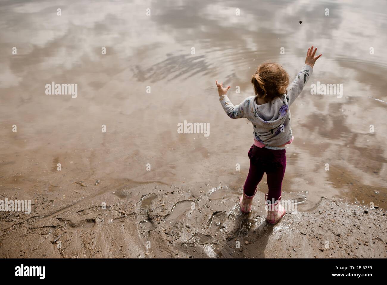 Ragazza toddler in stivali da pioggia gettando roccia nel lago dentro l'estate Foto Stock