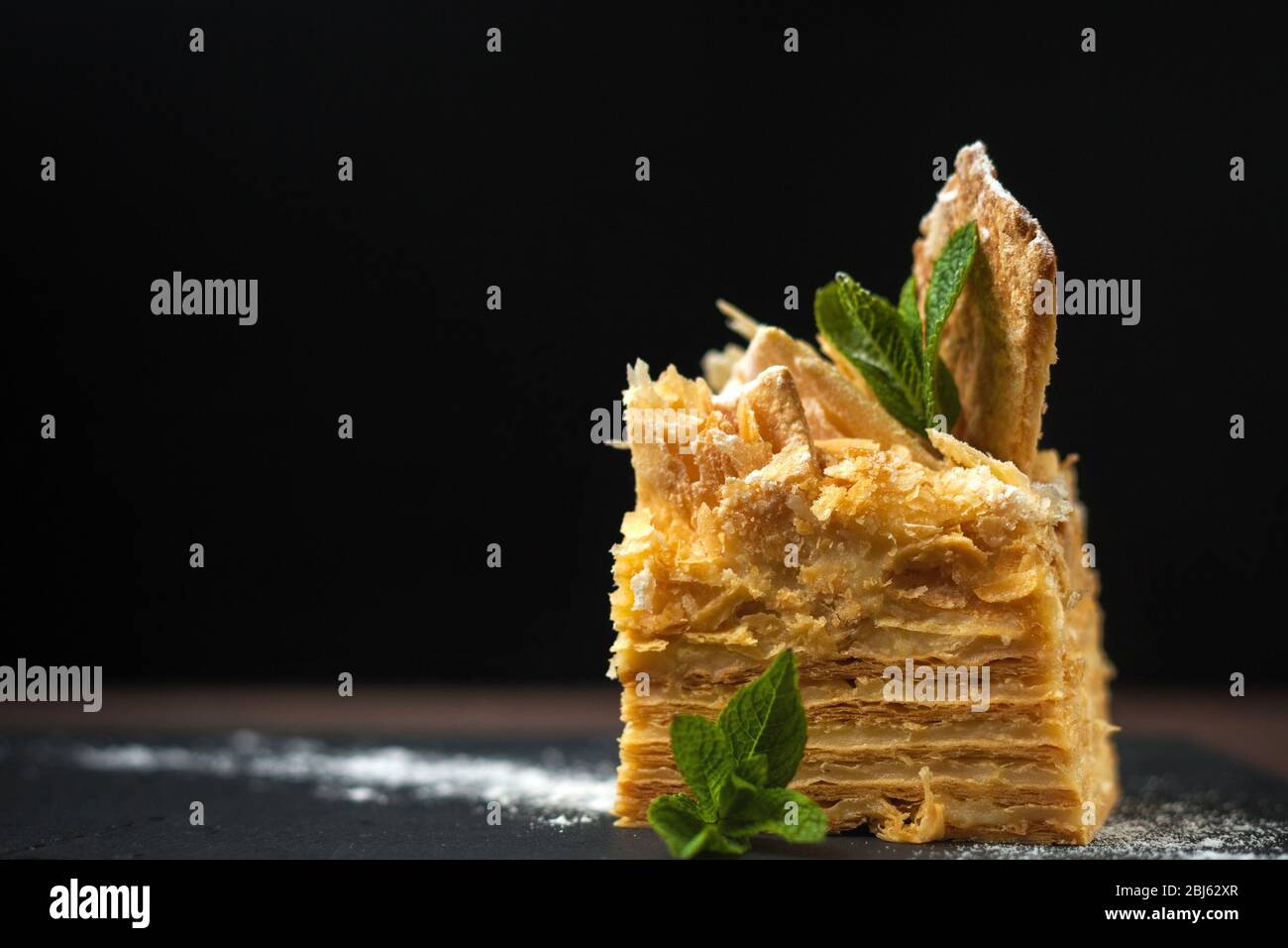 Torta di Napoleone con crema pasticcera e foglie di menta. Per il menu del cafe'. Area di testo per la progettazione. Con sfondo nero. Foto Stock