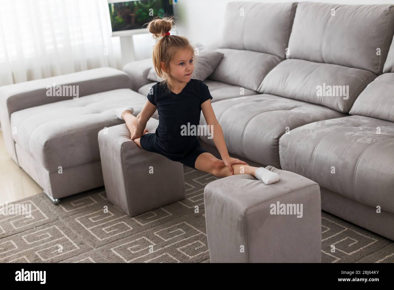 la piccola ginnastica in quarantena a casa durante una lezione online si divide sui polsini Foto Stock