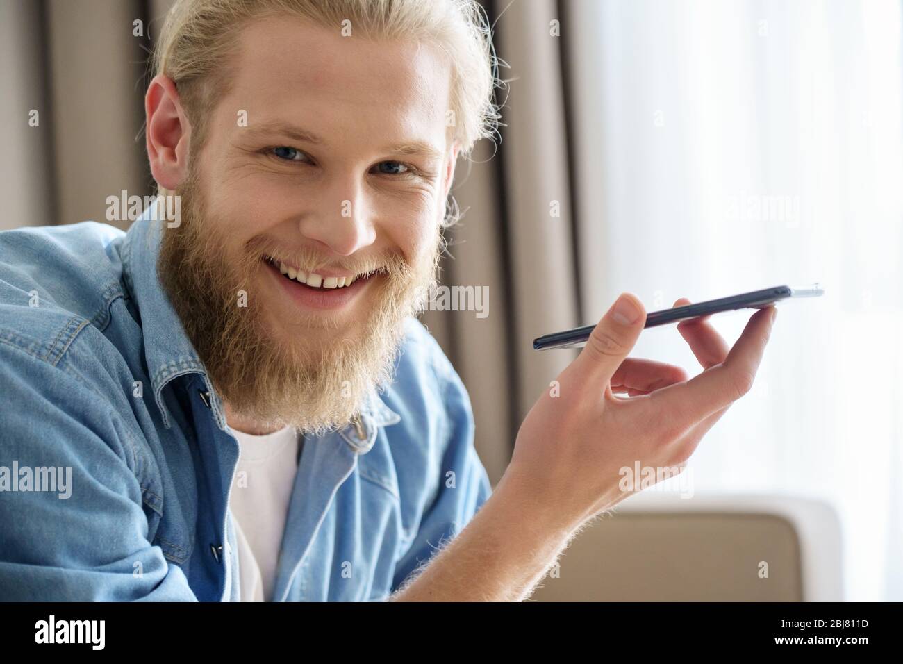 Buon giovane che tiene il telefono con l'assistente vocale virtuale guardando la macchina fotografica. Foto Stock