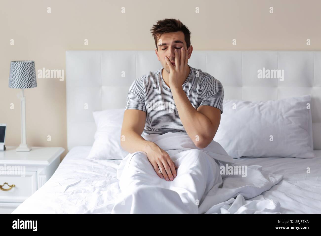 Giovane uomo assonnato che sfrega l'occhio a letto a casa Foto stock - Alamy