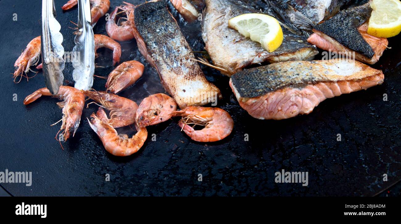 Primo piano di pesce alla griglia e gamberi su nero in padella all'aperto. Vista dall'alto Foto Stock