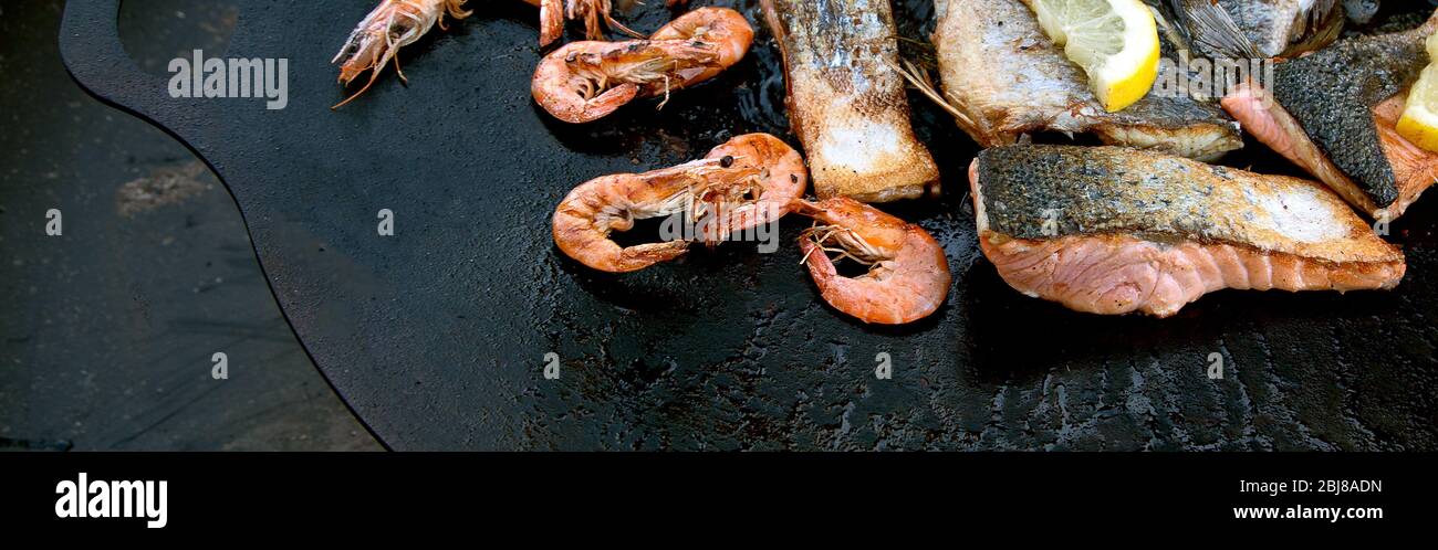 Primo piano di pesce alla griglia e gamberi su nero in padella all'aperto. Vista dall'alto, panorama, banner Foto Stock
