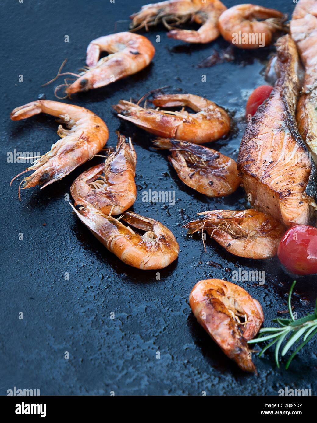 Primo piano di pesce alla griglia e gamberi su nero in padella all'aperto. Vista dall'alto Foto Stock