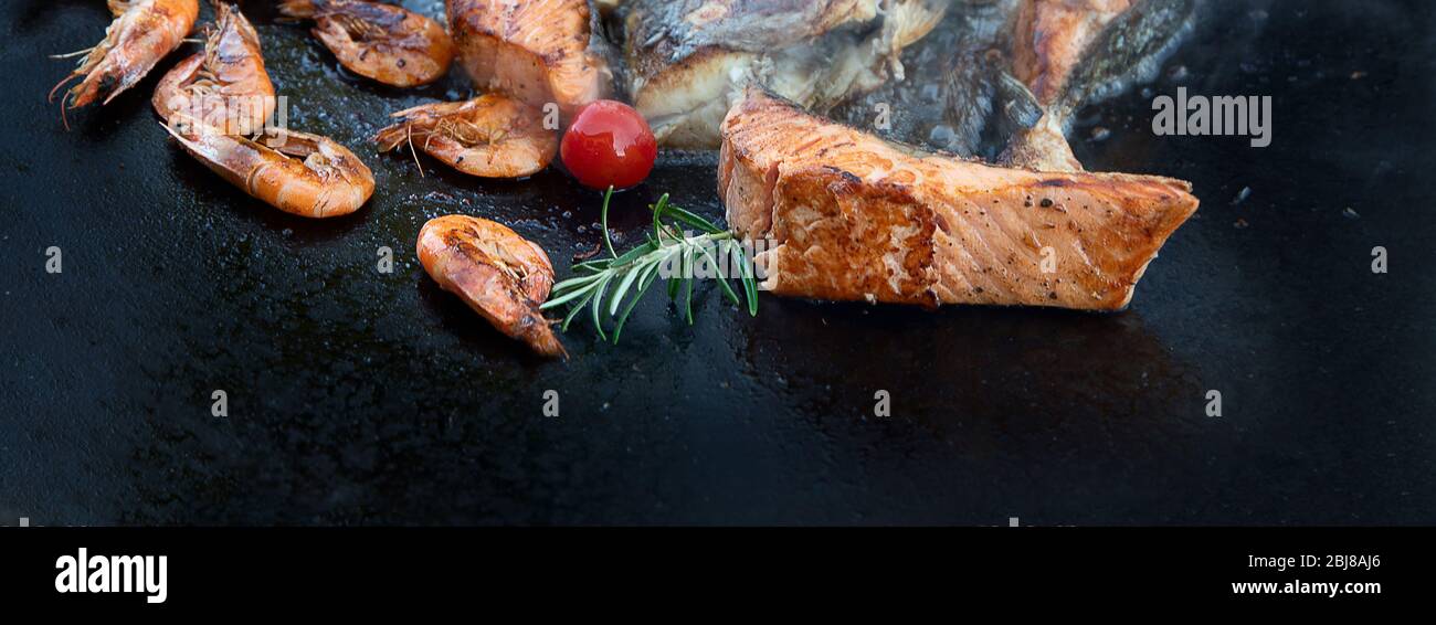 Primo piano di pesce alla griglia e gamberi su nero in padella all'aperto. Vista dall'alto Foto Stock