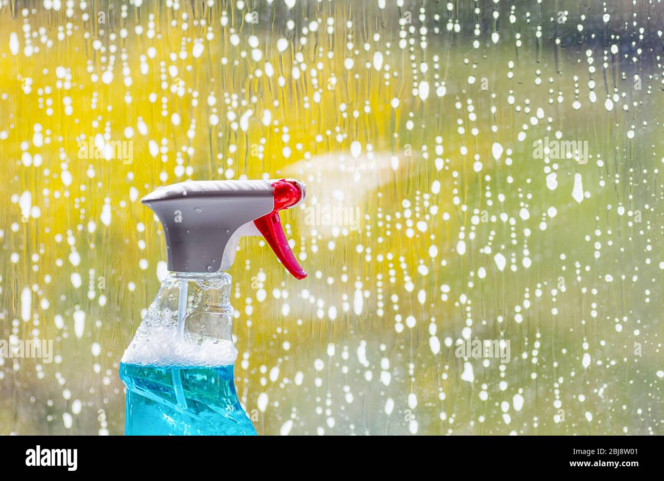 Detergente per vetri in una bottiglia di plastica con spray, sullo sfondo di una finestra. Concetto di pulizia della molla. Primo piano. Foto Stock