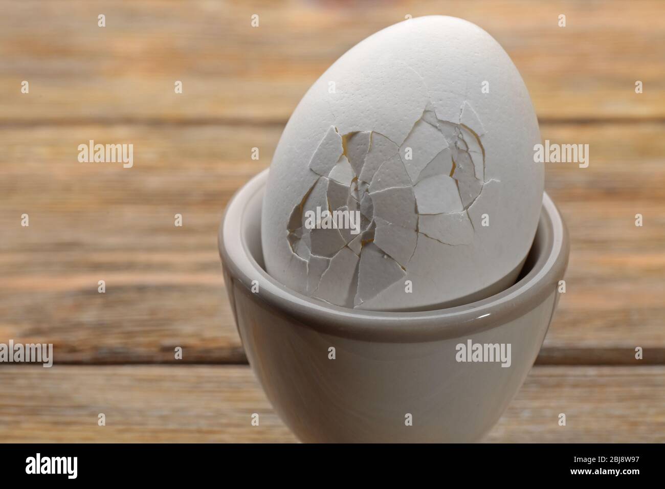 Uovo cracked in tazza di uovo su sfondo di legno Foto Stock