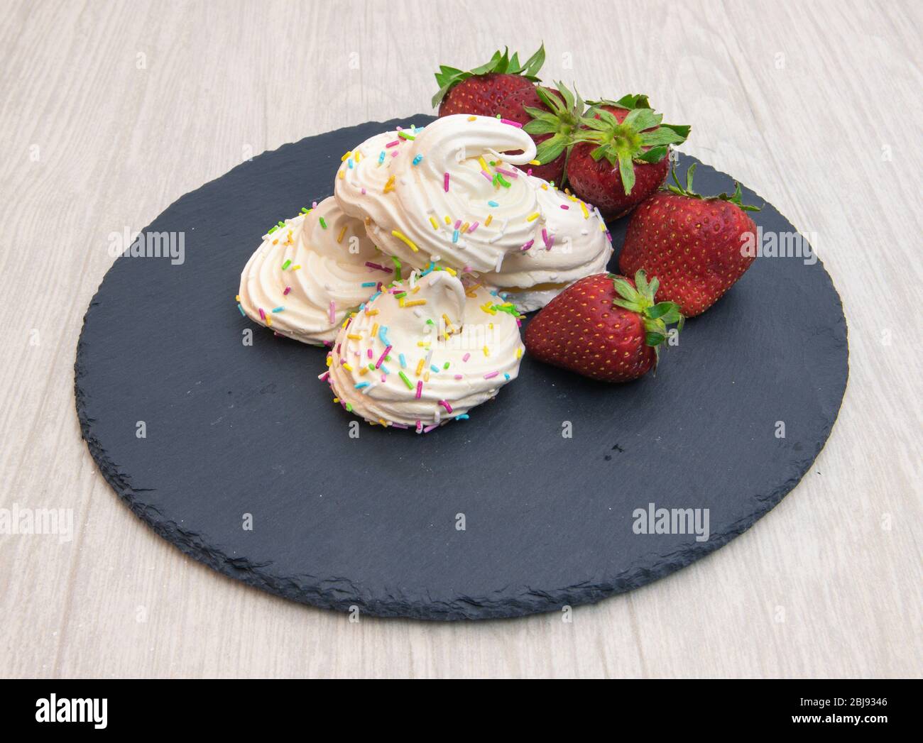 meringhe con fragole su piatto nero e fondo bianco Foto Stock