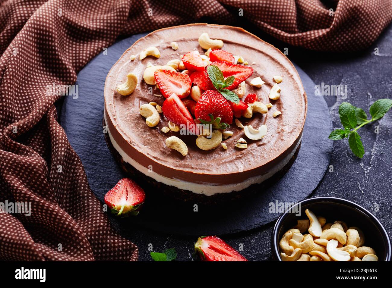 Semplice torta al cioccolato senza forno fatta di crema di cocco e anacardi imbibiti con la crosta di datteri crudi, cacao e pecan con fragole e fre Foto Stock