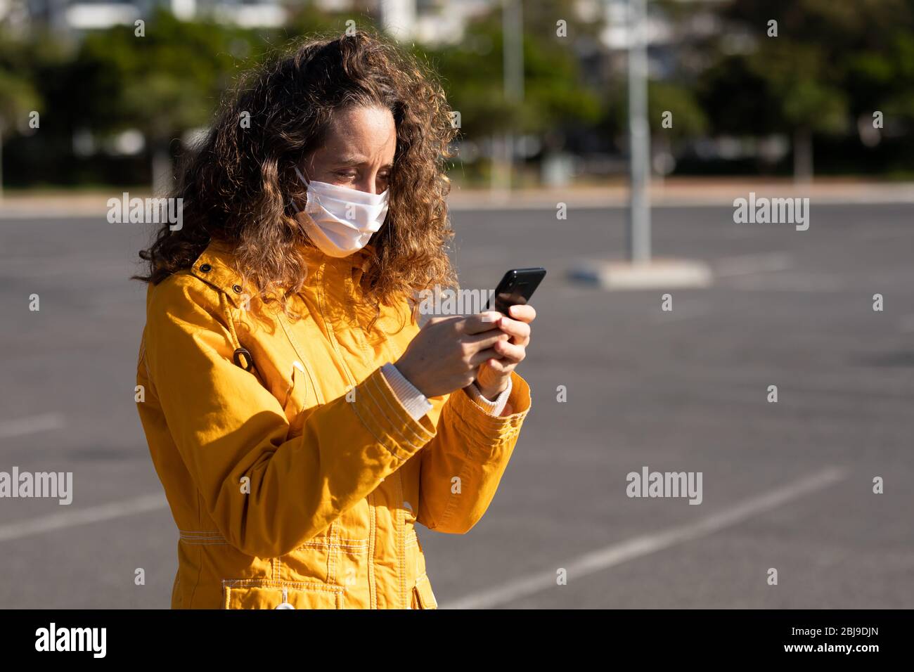 Donna caucasica che indossa una maschera protettiva per le strade e usa il suo telefono Foto Stock