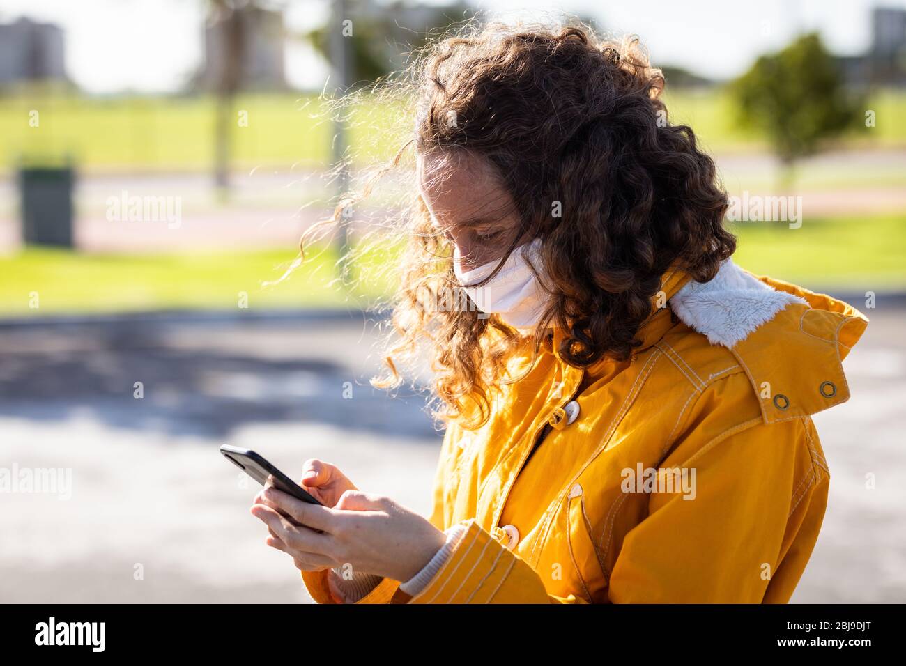 Donna caucasica che indossa una maschera protettiva per le strade e usa il suo telefono Foto Stock