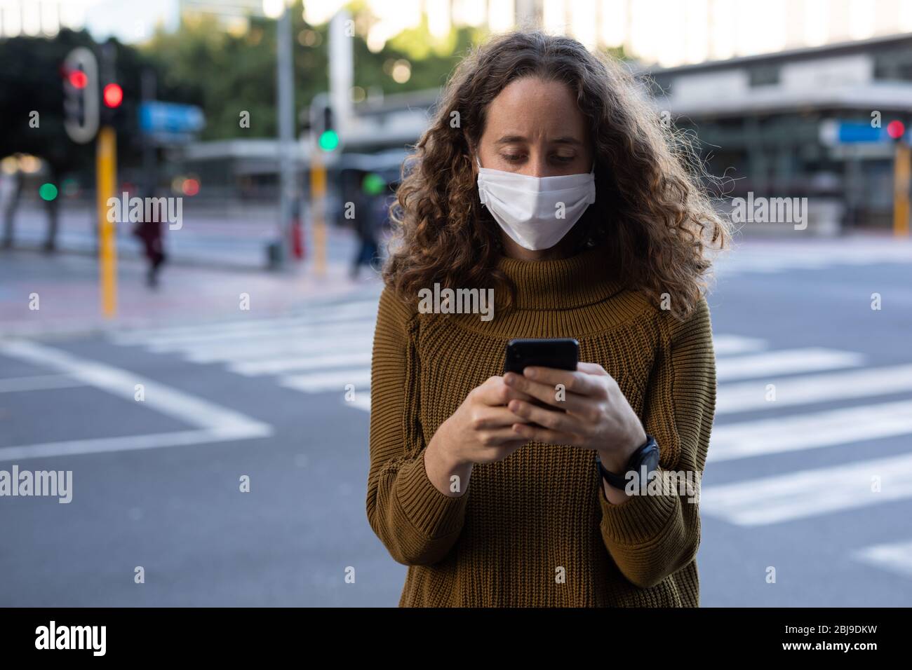 Donna caucasica che indossa una maschera protettiva e usa il suo telefono per le strade Foto Stock