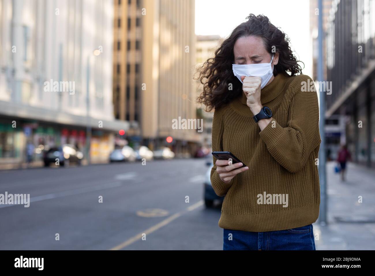 Donna caucasica che indossa una maschera protettiva e tosse fuori per le strade Foto Stock