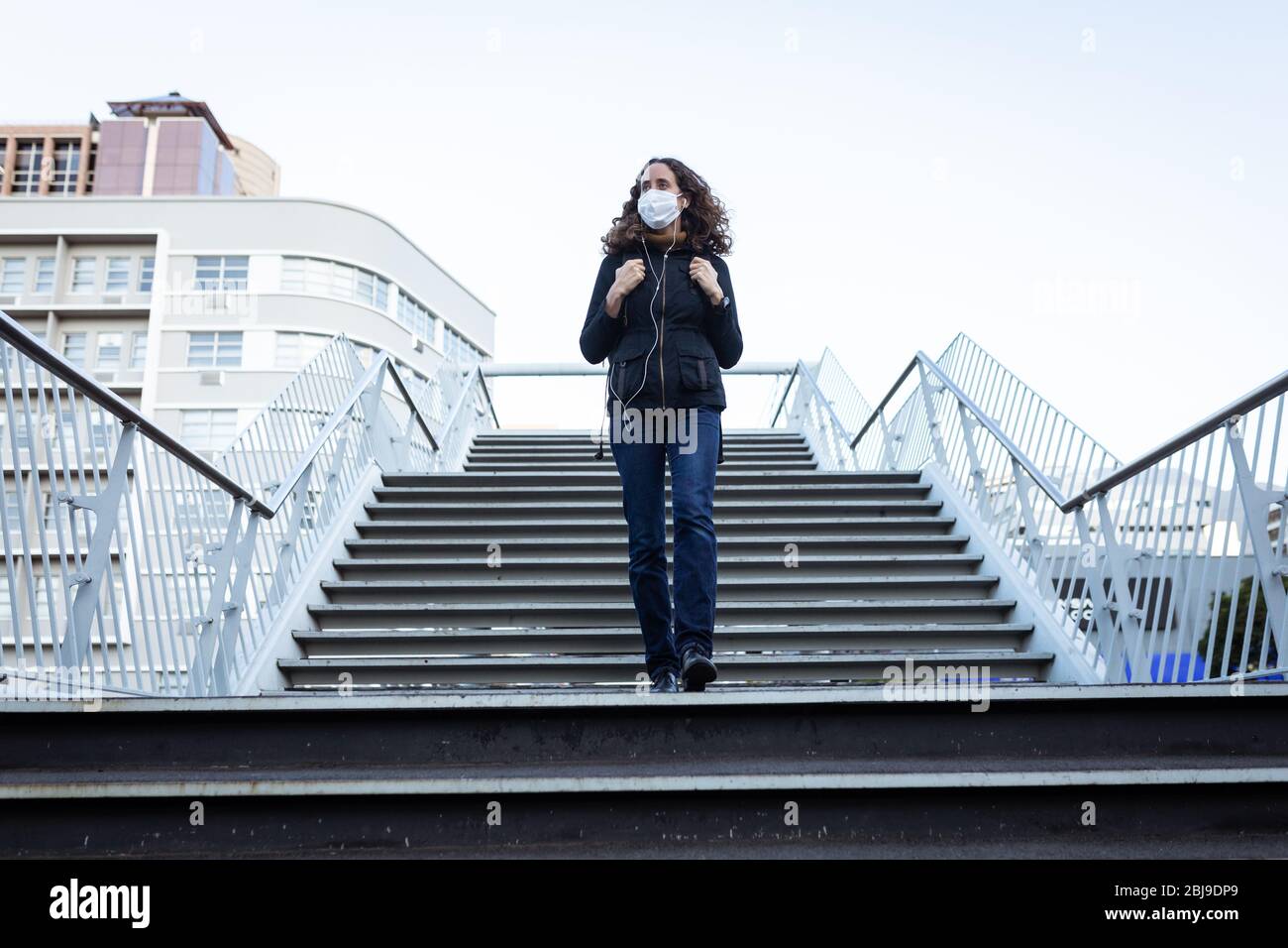 Donna caucasica che indossa una maschera protettiva e scende le scale Foto Stock
