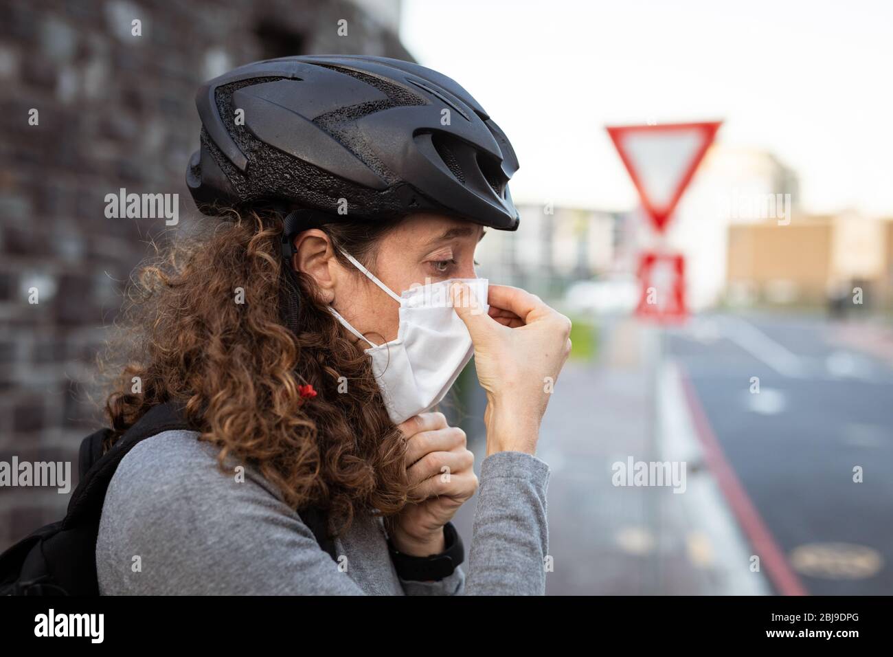 Donna caucasica indossare una maschera protettiva e un casco per biciclette per le strade Foto Stock